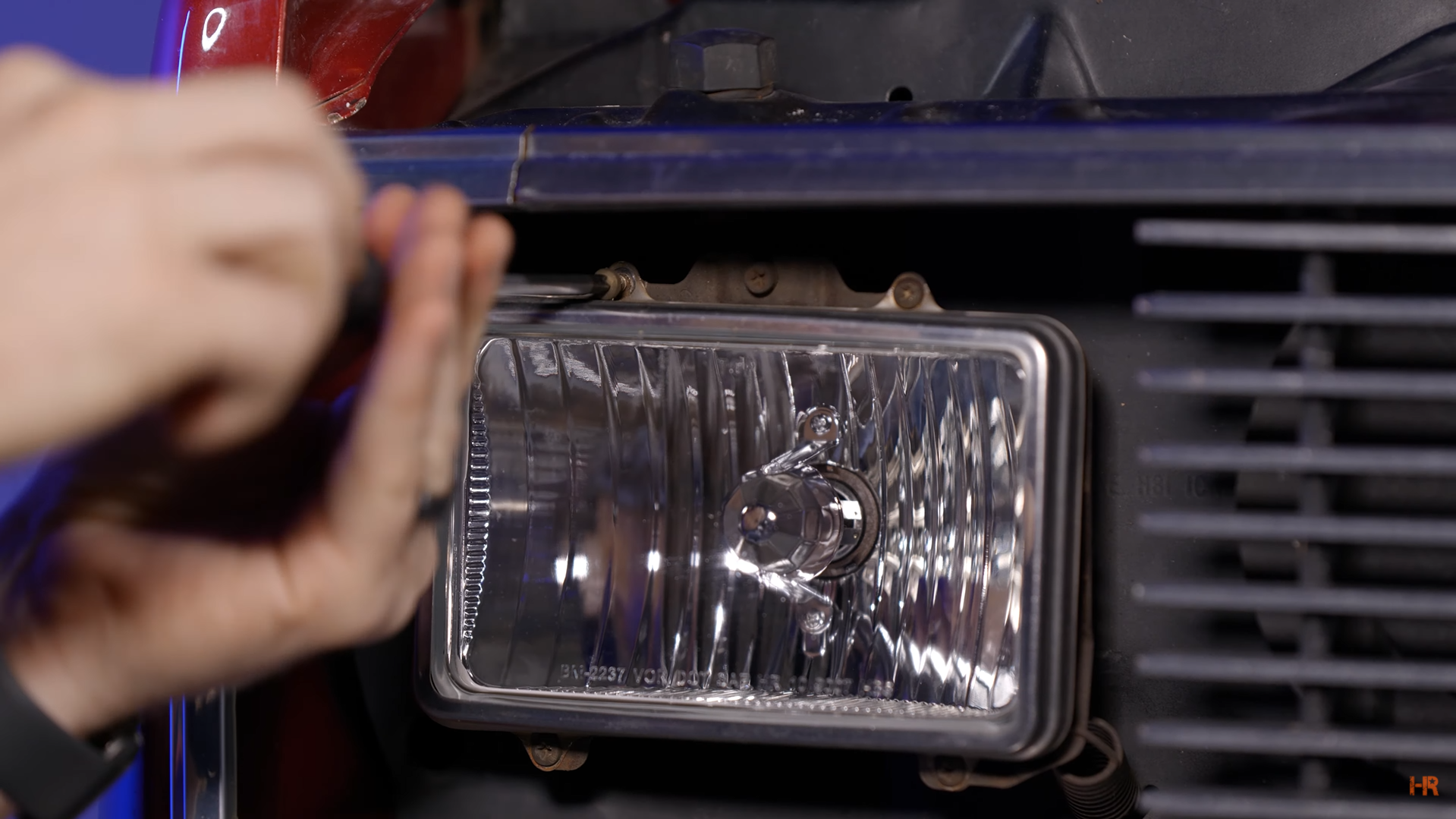 A man is unscrewing the retainer ring that holds in the OEM headlight.