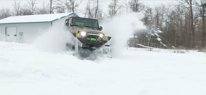 A Jeep Wrangler TJ with half-tracks attached driving in the snow.