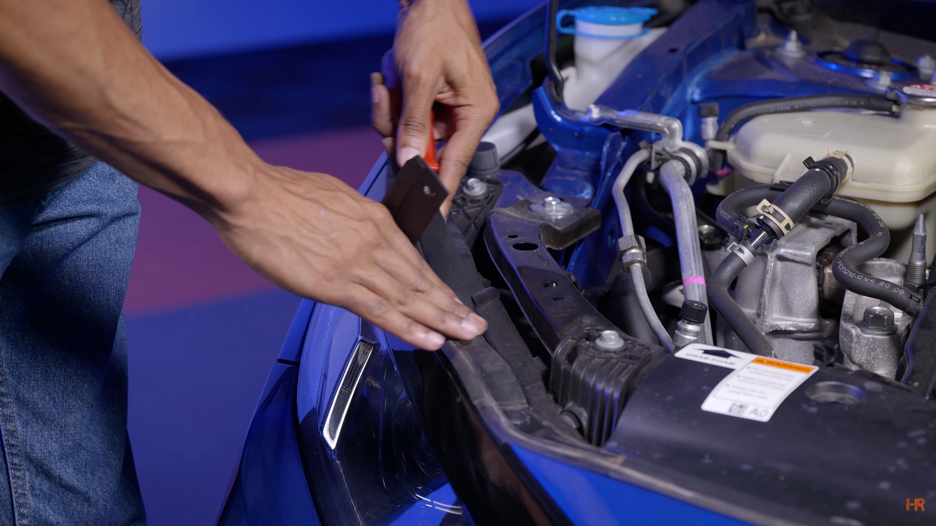 A man removes the rubber bushing along the front of a Honda Civic's engine bay.
