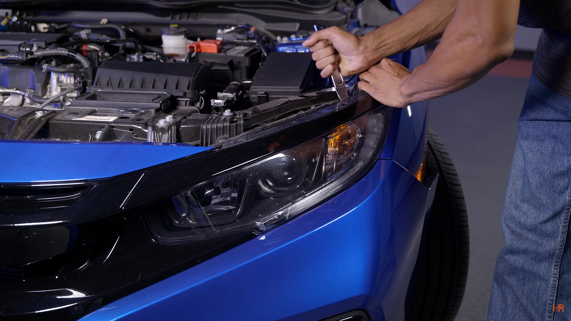 A man uses a pry tool to remove the stock headlights from a Honda Civic.
