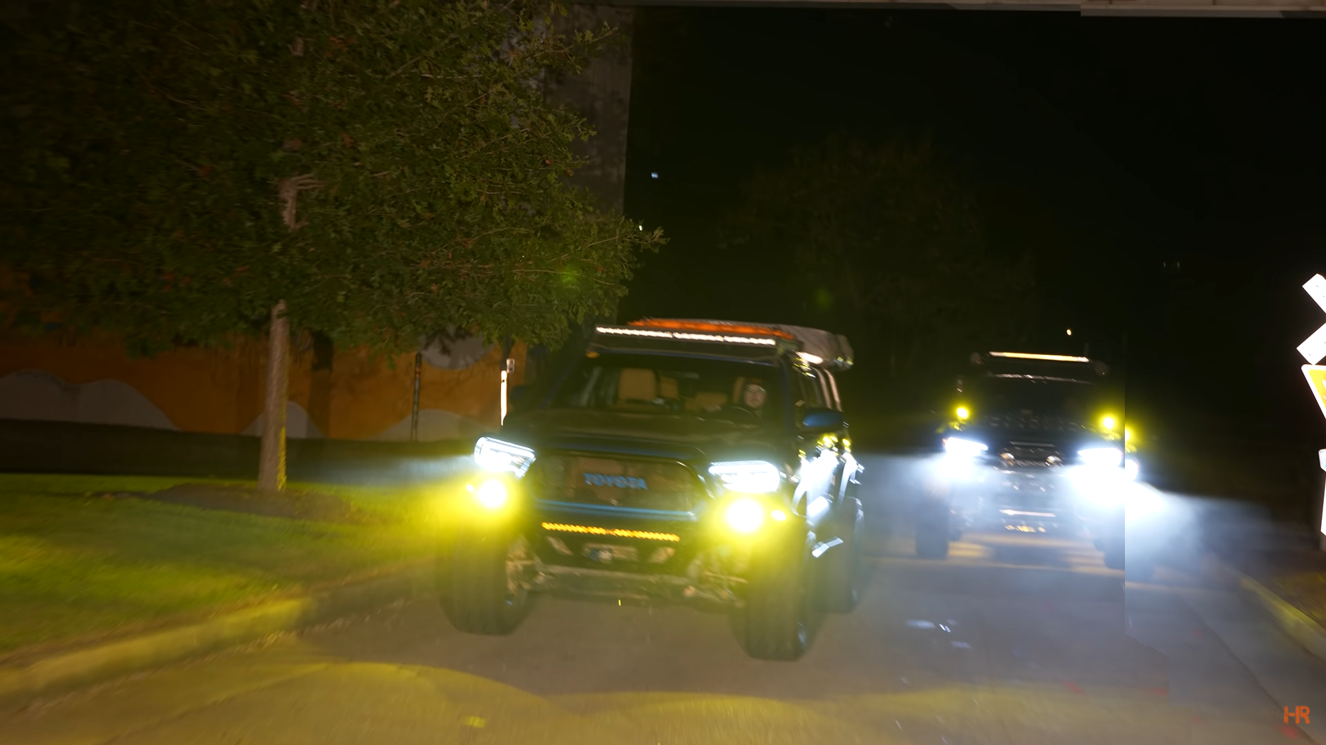 Two Toyota Tacoma's drive with yellow fog lights on.